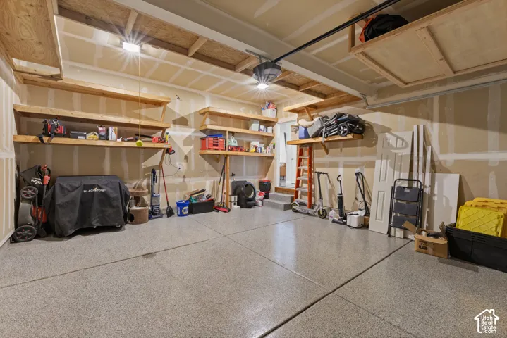 Garage featuring epoxy-coated concrete flooring, custom built-in wooden wall shelving, and overhead storage platforms