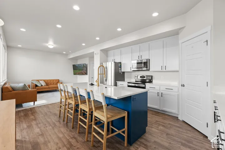 Kitchen featuring white shaker-style cabinetry, quartz countertops, a contrasting navy blue center island, stainless steel appliances, and wood-finish flooring