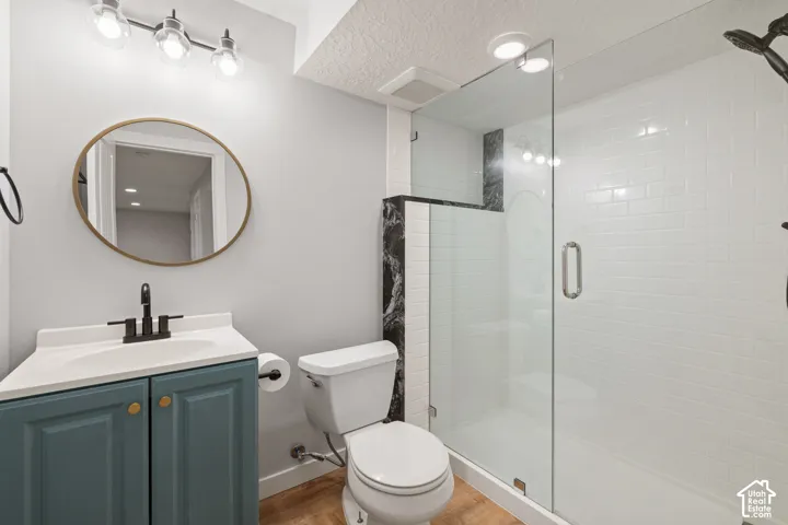 Bathroom featuring a vanity with a white countertop and matte black faucet, oval wall mirror, wood-finish flooring, and a walk-in shower with white subway tile, dark stone-finish accents, and a glass door