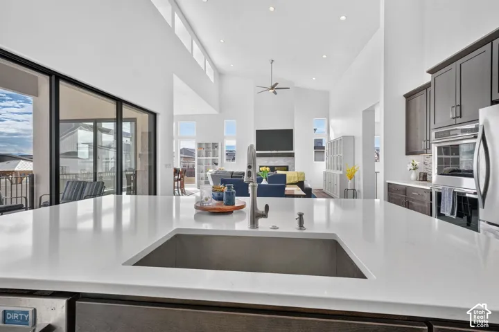 Kitchen island featuring a quartz countertop and an undermount stainless steel sink with a high-arch faucet, complemented by dark wood cabinetry, stainless steel double wall ovens, and soaring vaulted ceilings