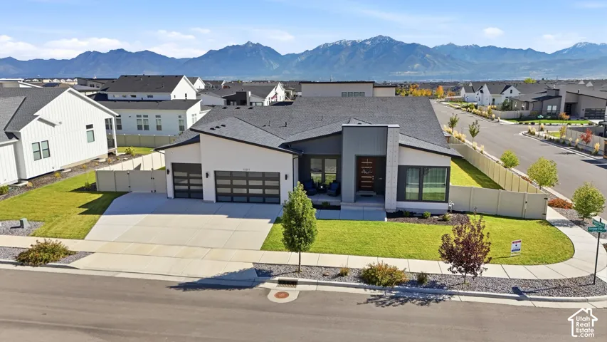 Modern architectural exterior featuring a mixed-material facade, multi-car garage with glass-panel doors, landscaped lawn, and a prominent mountain backdrop