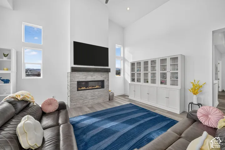 Vaulted ceiling featuring a linear fireplace with stacked stone surround, dark wood mantel, wood-finish flooring, and floor-to-ceiling built-in cabinetry with glass-front display doors