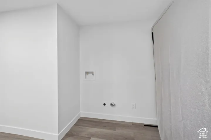 Dedicated utility space featuring recessed plumbing connections, wood-finish flooring, and crisp white wall finishes