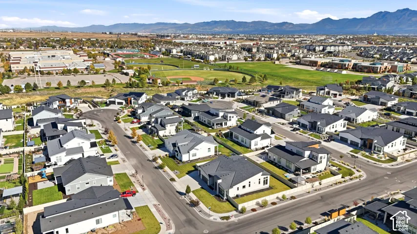 Aerial perspective of the residential community featuring dark-pitched rooflines, paved street infrastructure, manicured corner lots, and a backdrop of distant mountain ranges