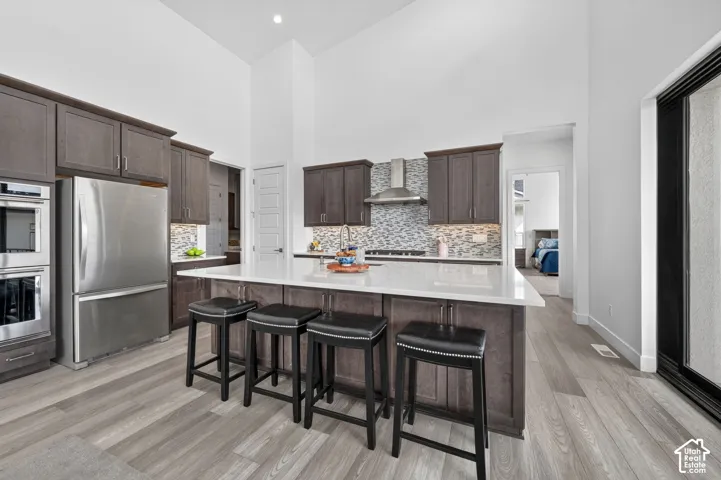 Kitchen featuring vaulted ceilings, dark wood-finish cabinetry, a large center island with a stone-composite countertop, stainless steel appliances, and a mosaic tile backsplash