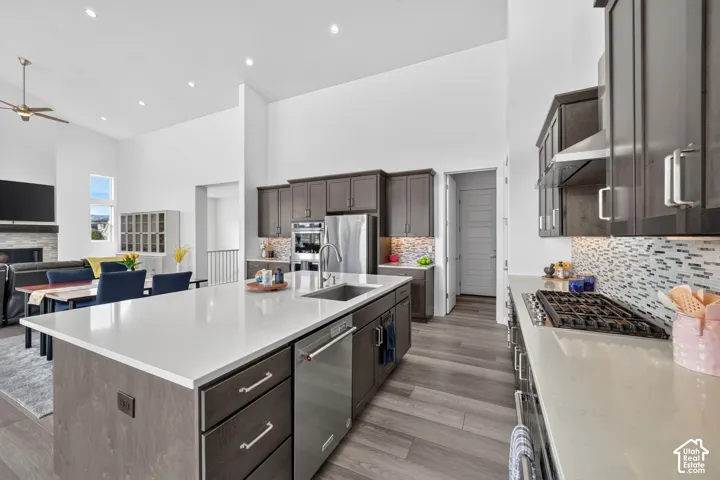Kitchen featuring custom dark wood cabinetry, light-toned stone countertops, a large central island with stainless steel undermount sink, gas range, and wood-finish flooring