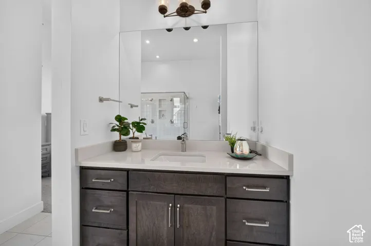 Vanity featuring dark-stained wood cabinetry, light-toned composite countertop with an integrated rectangular sink, wall-spanning mirror, and three-bulb brushed-nickel light fixture