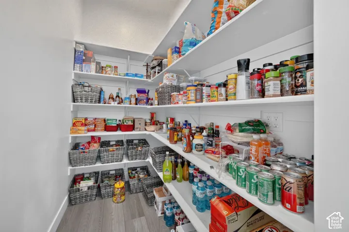 Walk-in pantry featuring white custom built-in shelving, horizontal shiplap wall detailing, and wood-finish flooring
