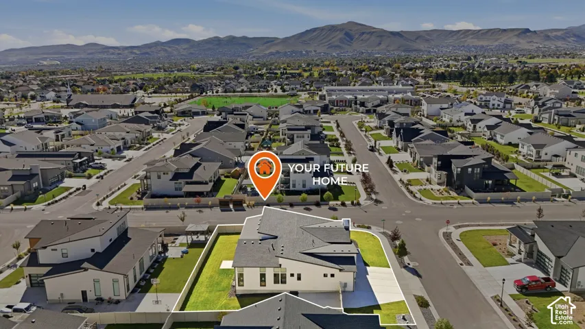 Aerial perspective featuring a corner-lot property with a fenced yard, expansive lawn, concrete driveway, and mountain scenery