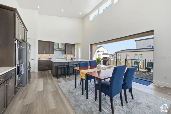 Open-concept kitchen and dining area featuring high ceilings, dark-finish cabinetry, a large center island, and a wide sliding door opening to a balcony