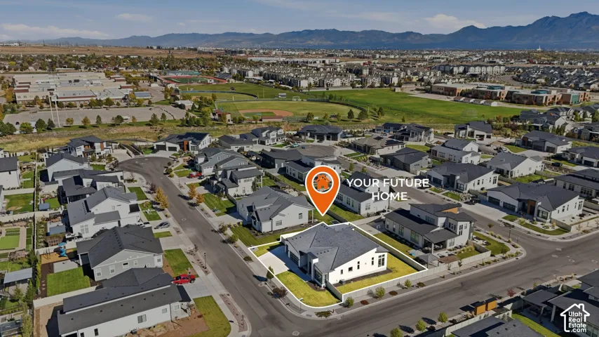 Aerial perspective of a corner lot residence featuring a multi-pitch roof, an attached garage, and a backdrop of mountain scenery