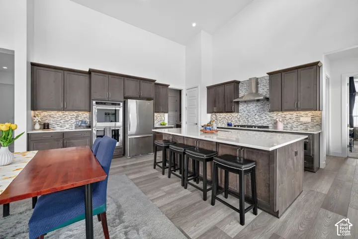 Kitchen featuring vaulted ceilings, dark stained cabinetry, quartz countertops, a stone-patterned backsplash, and stainless steel double wall ovens