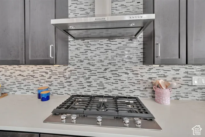 Kitchen featuring dark cabinetry, a gas cooktop, stainless steel ventilation hood, and mosaic tile backsplash