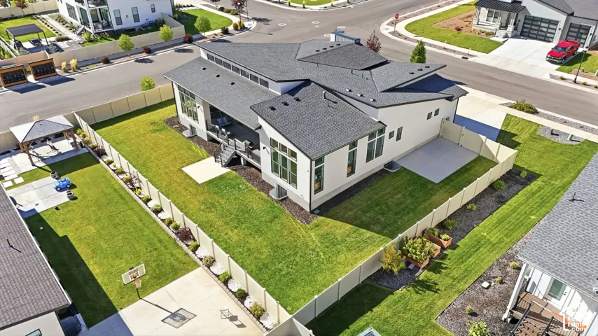 Modern residence featuring a multi-pitched roofline, light-toned exterior finish, large windows with transom detailing, an elevated rear deck, and a fenced yard with a concrete patio