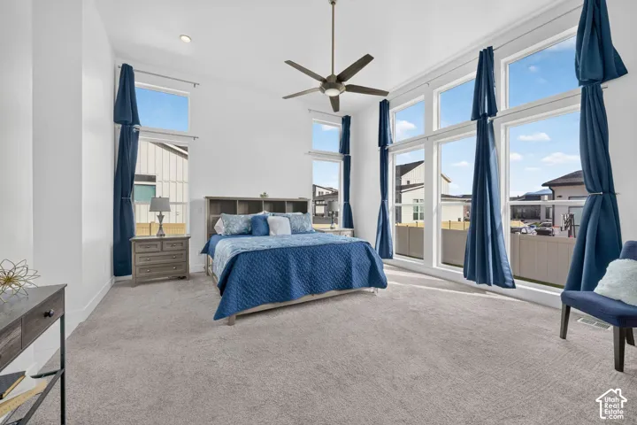 High-ceilinged room featuring expansive multi-pane windows, carpeted flooring, and a ceiling-mounted fan