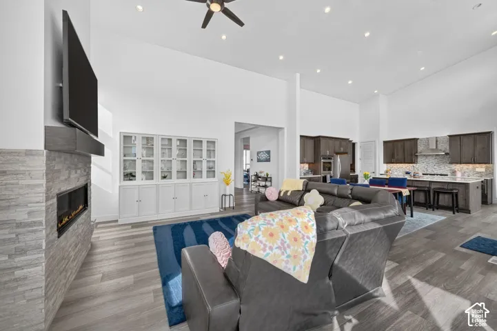 Open-concept area featuring high ceilings, wood-finish flooring, a stone-surround fireplace with built-in mantel, and custom white cabinetry with glass-front display doors