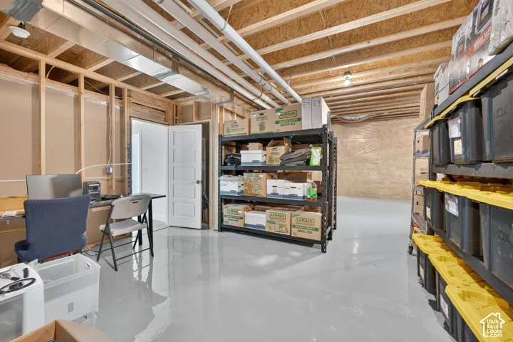 Unfinished lower level featuring exposed wood joist ceilings, light-reflective epoxy floor coating, metal HVAC ductwork, and an interior five-panel door