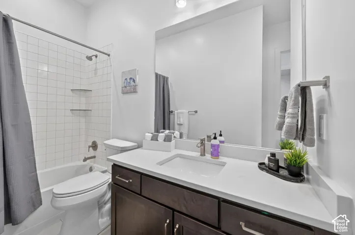 Bathroom featuring a dark wood-finish vanity with a light-toned countertop, integrated rectangular sink, large wall-mounted mirror, and a tub-shower combination with square wall tile and built-in glass shelving