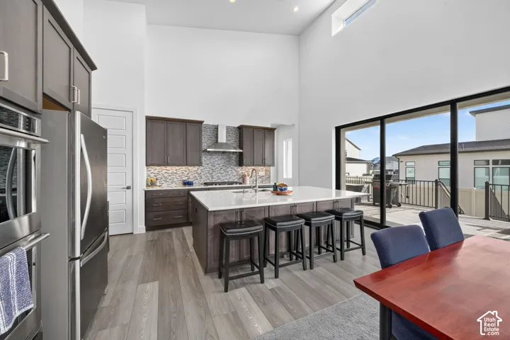 Kitchen featuring high ceilings, a central island with a quartz countertop, wood-finish flooring, dark-toned cabinetry, and a full-height window wall