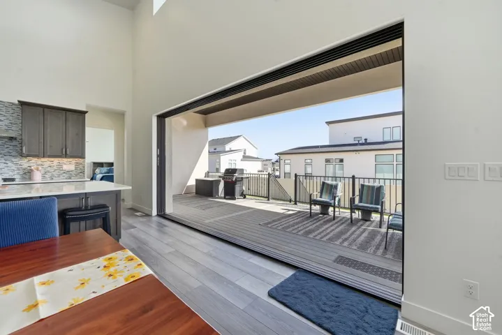 Large-format sliding glass wall system opening to an expansive balcony with metal railing, vaulted ceilings, kitchen island with stone countertop, and wood-finish flooring