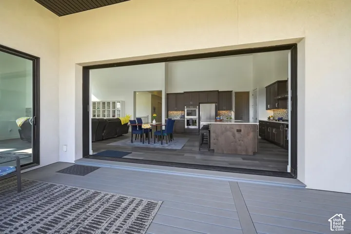 Covered outdoor deck with composite decking featuring expansive multi-panel sliding glass doors, dark wood-finish cabinetry, a large kitchen island, and built-in double wall ovens