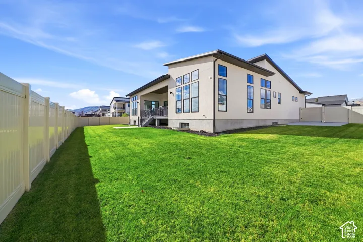 Stucco exterior featuring multi-pane windows, a covered rear patio, a vinyl privacy fence, and a concrete foundation