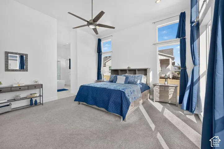 High ceilings, floor-to-ceiling windows, neutral carpet flooring, and a multi-blade ceiling fan with integrated lighting