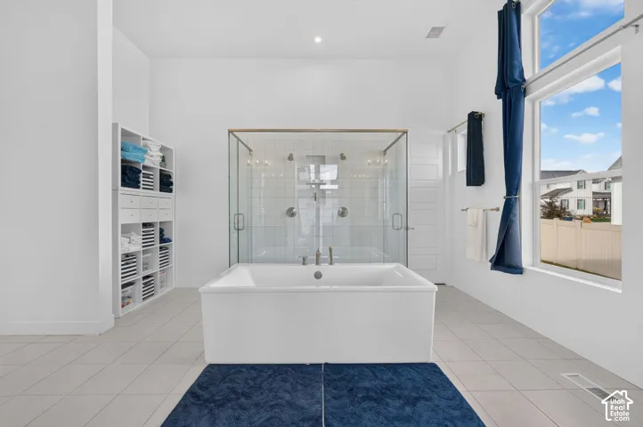 High-ceiling bathroom featuring a deep-profile soaking tub, glass-enclosed shower with dual showerheads, built-in white shelving, and large-format tile flooring