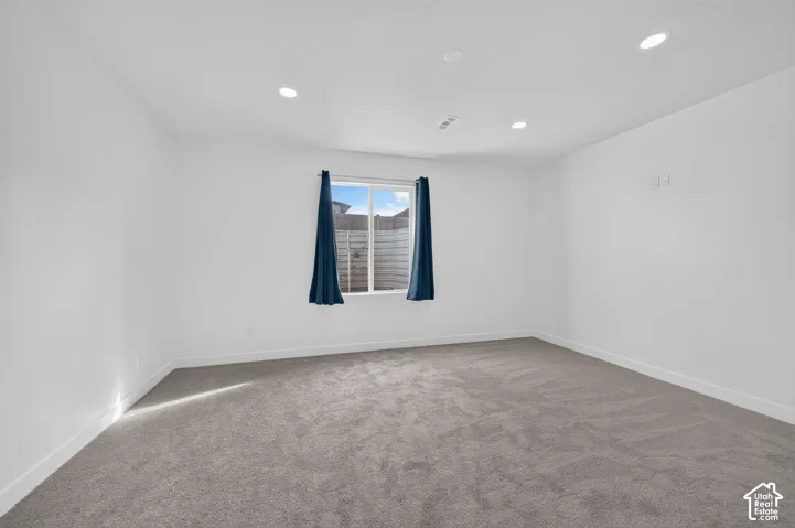 Neutral-toned interior space featuring wall-to-wall carpeting, recessed ceiling lighting, and a window with a view of exterior fencing