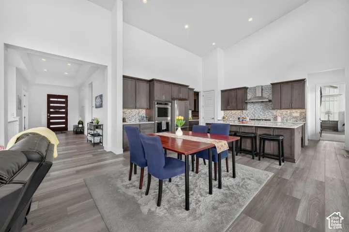 Kitchen featuring soaring vaulted ceilings, wood-finish flooring, dark wood cabinetry, a stone tile backsplash, and a central island with integrated seating