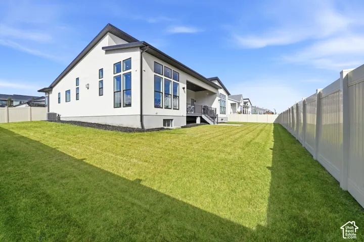 Rear exterior featuring light-toned stucco siding, oversized windows, an elevated covered patio, and a fenced backyard with lawn