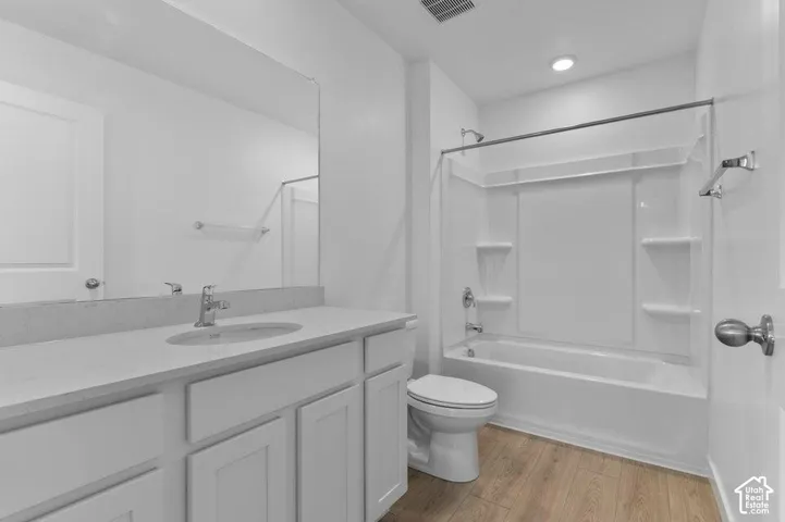 Bathroom featuring a vanity with a light-toned countertop, integrated basin, wood-finish flooring, and a tub-shower combination with built-in shelving