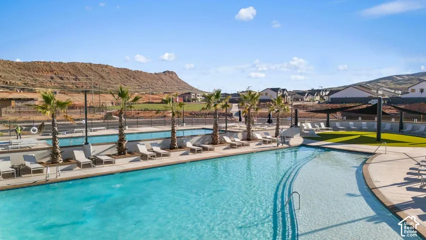 Resort-style swimming pool featuring a zero-entry access point, concrete decking, mature palm trees, and mountain scenery