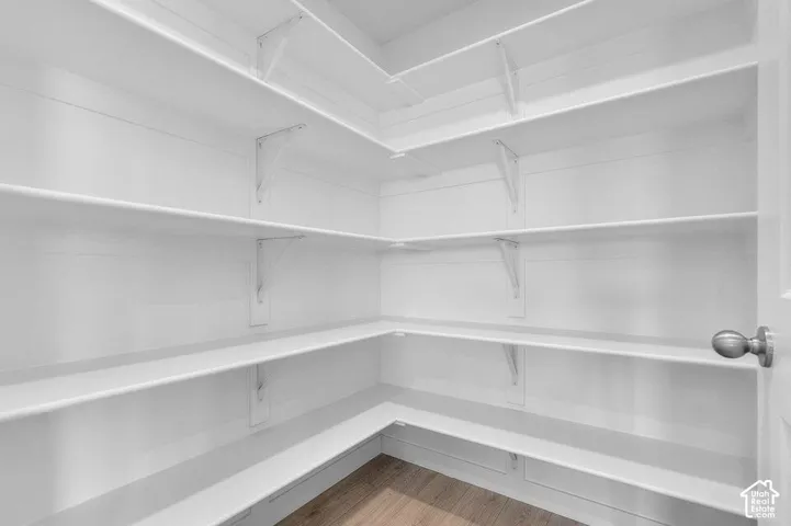 Walk-in storage featuring multi-level wrap-around shelving, white-finished wall paneling, and wood-finish flooring