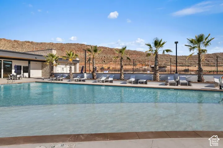 Swimming pool with a tanning ledge, concrete decking, stone-accented building exterior, and palm tree landscaping set against a rock formation backdrop