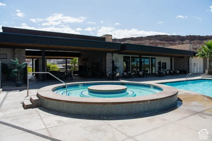 Circular in-ground spa with stone-tile surround, expansive concrete pool deck, integrated swimming pool, covered outdoor pavilion, and stone exterior accents