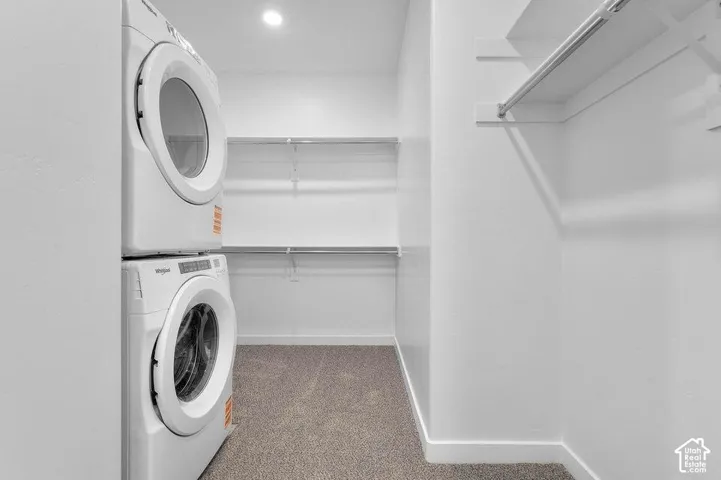 Dedicated laundry room featuring stacked front-load washers and dryers with modern white finishes, neutral tile flooring, recessed lighting, and built-in shelving for storage and organization