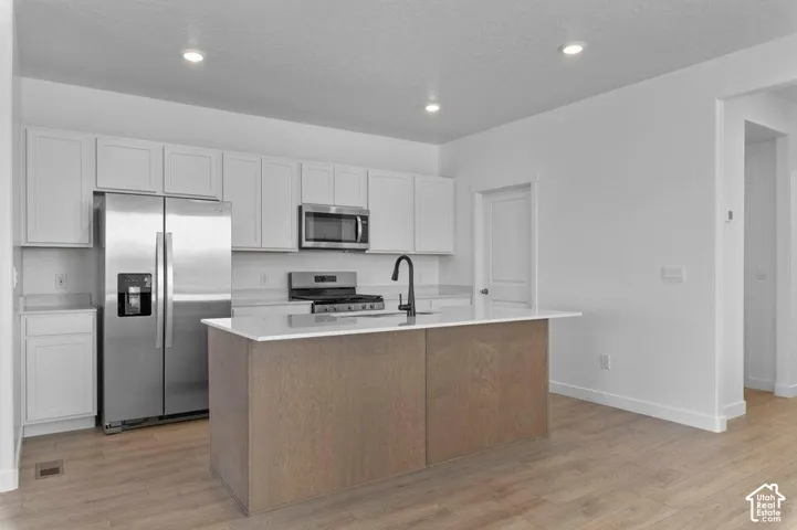 Kitchen featuring white shaker-style cabinetry, wood-finish flooring, a central island with a solid-surface countertop, stainless steel appliances, and a matte black faucet