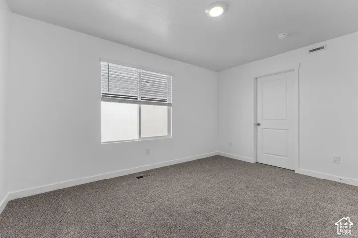 Neutral-toned wall-to-wall carpeting, crisp white walls, sliding window with horizontal blinds, and a solid-core interior door with satin nickel hardware