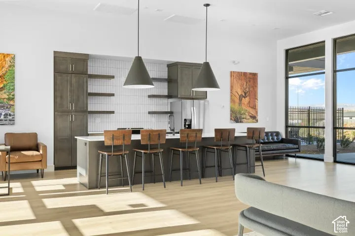 Kitchen featuring a central island with countertop seating, vertical tile backsplash, wood-finish cabinetry, open shelving, and dual pendant lighting