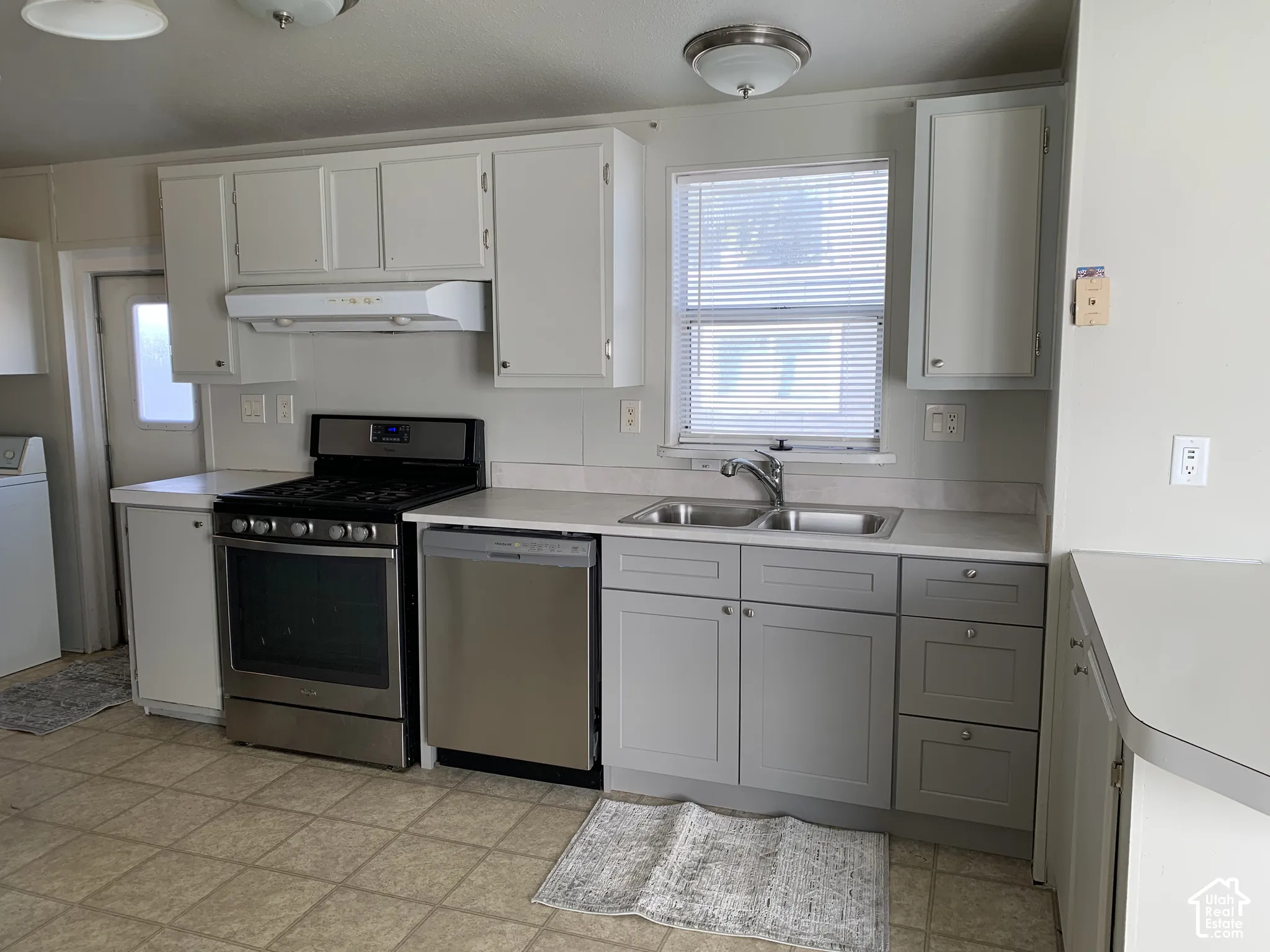 Kitchen featuring gray cabinetry, stainless steel range and dishwasher, dual-basin sink with pull-down faucet, and neutral flooring
