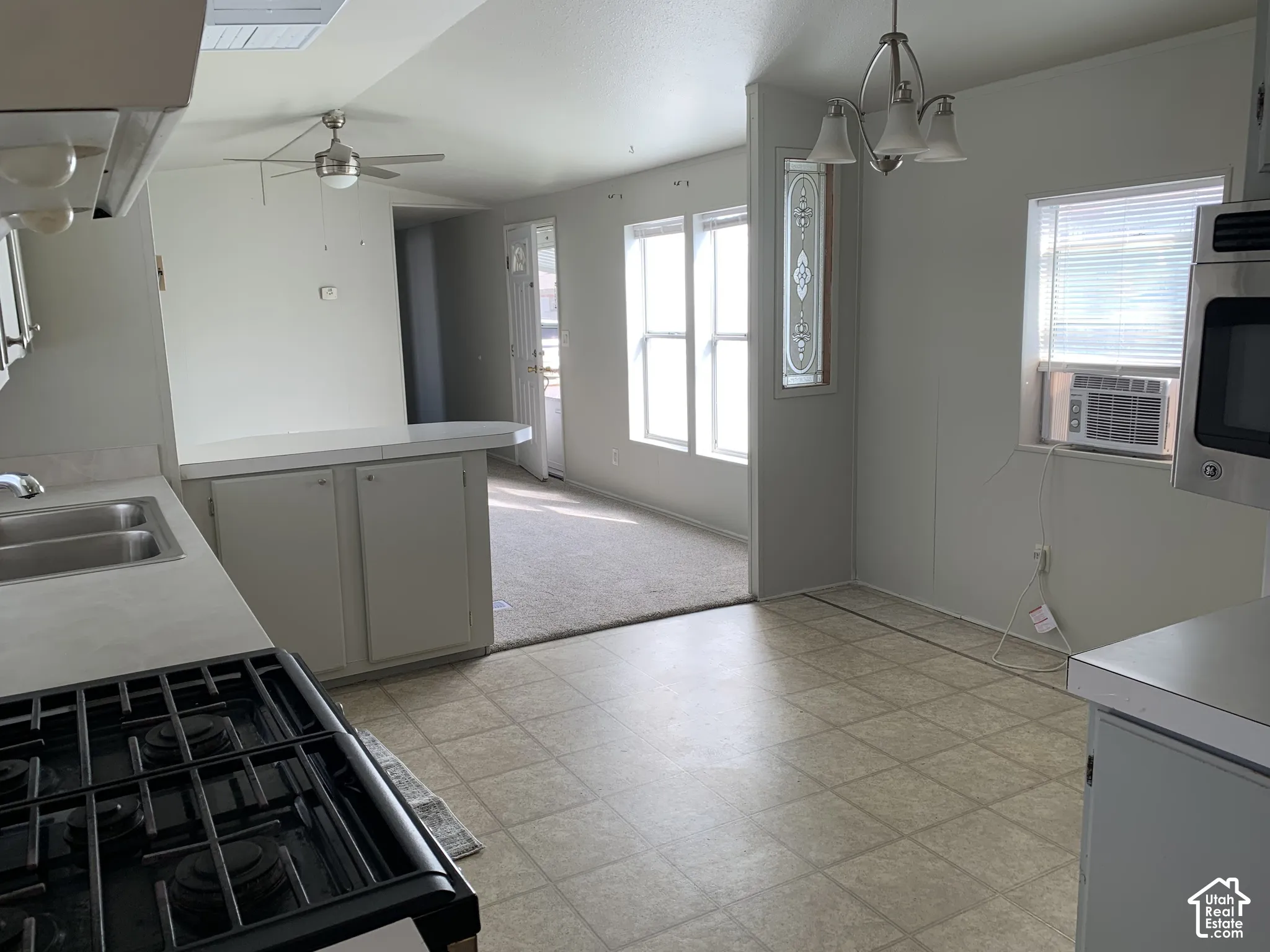 Kitchen featuring a gas range, dual-basin sink, peninsula cabinetry, neutral tile flooring, and a multi-light chandelier