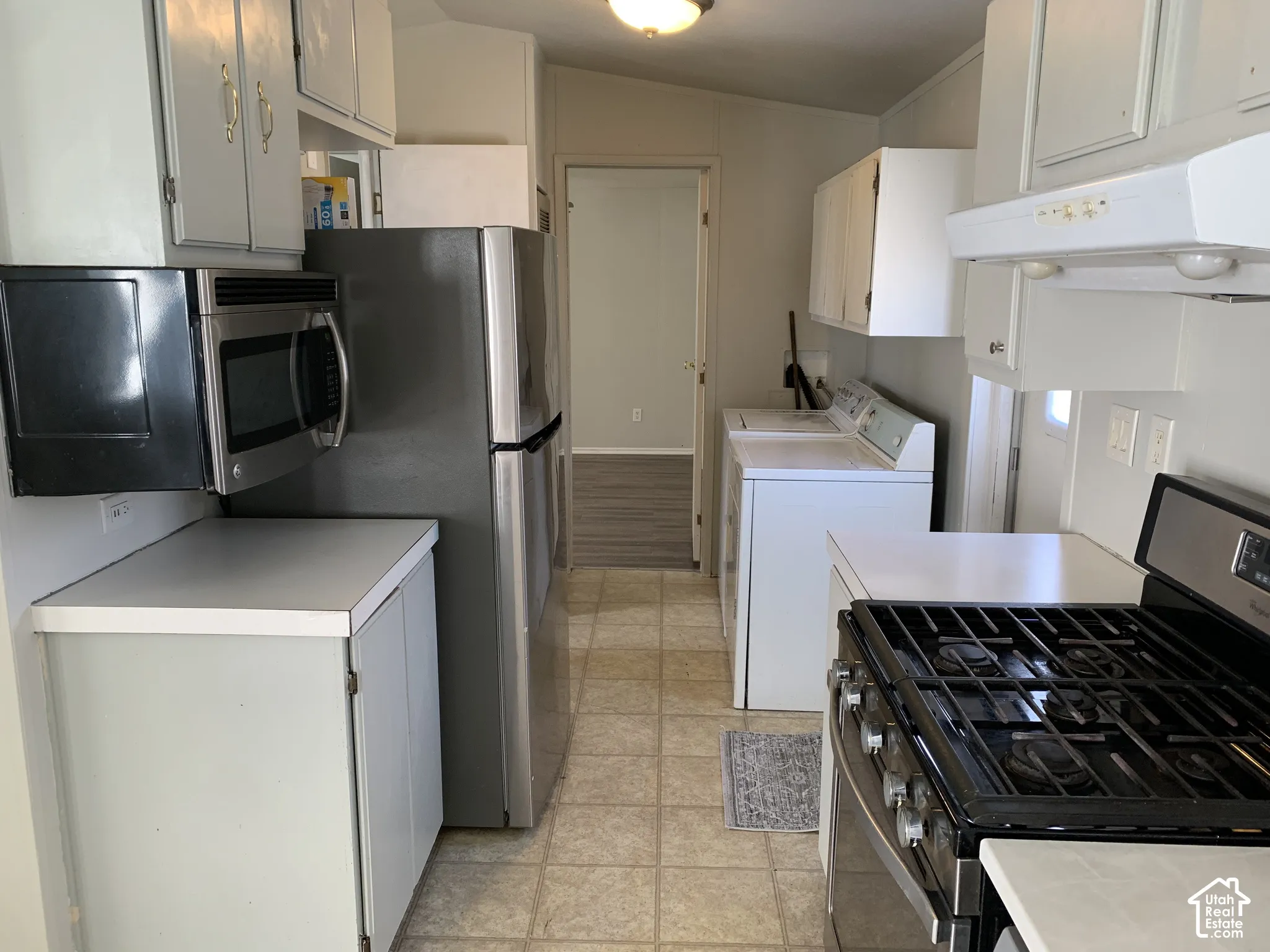 Kitchen featuring white cabinetry, new countertop, stainless steel microwave, refrigerator, and gas range
