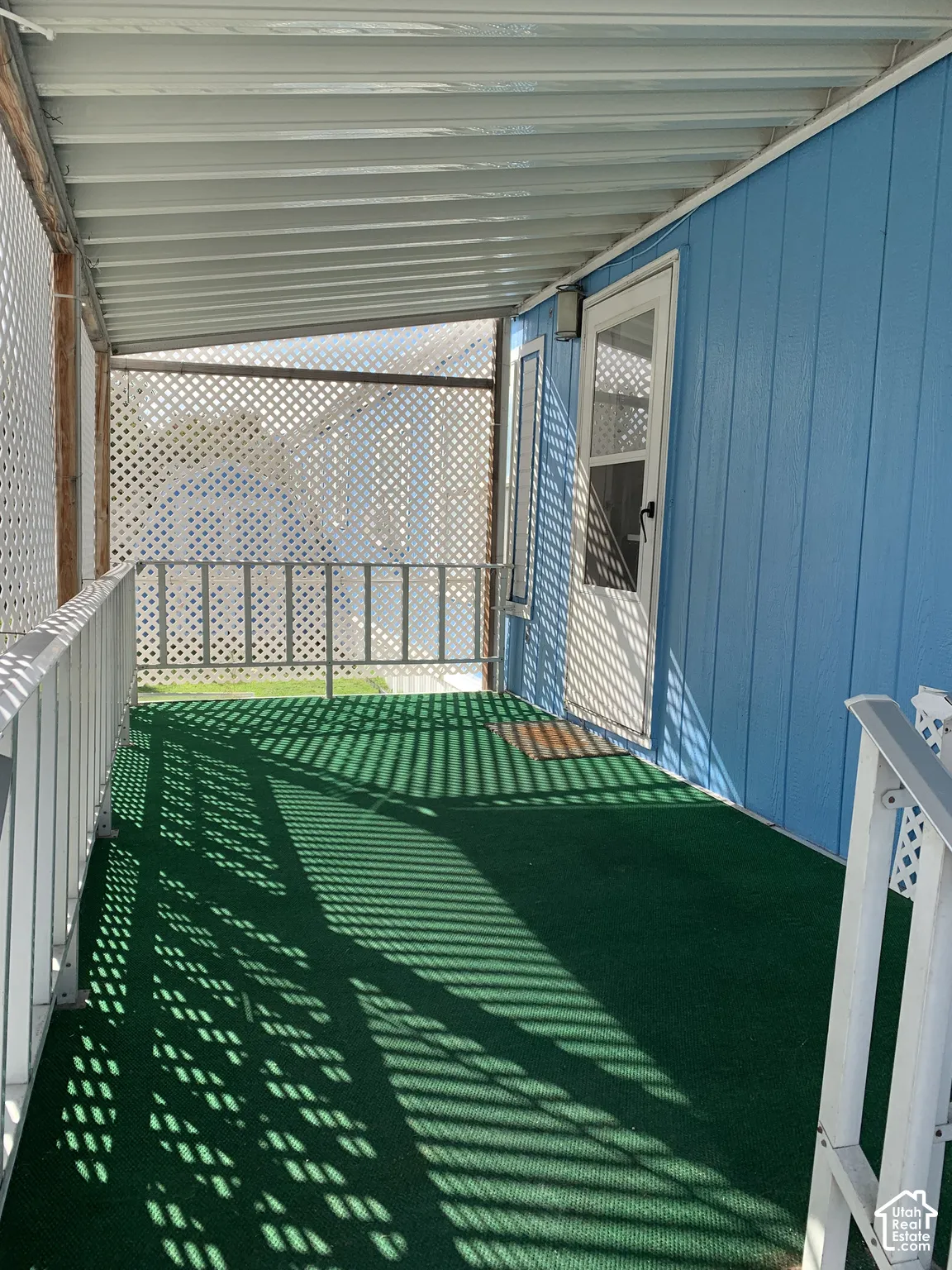 Covered porch featuring a paneled exterior, metal corrugated roof, perimeter lattice fencing, and metal railing