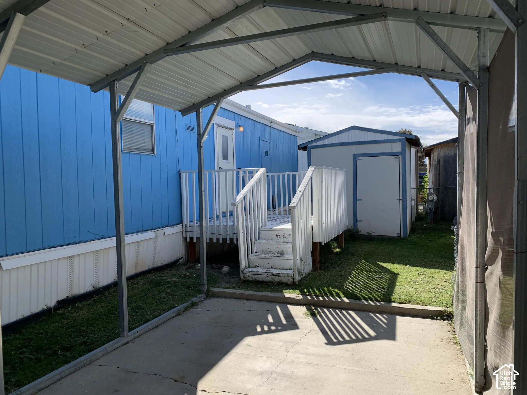 Covered carport with metal roof, raised wooden deck with railings, and detached storage shed