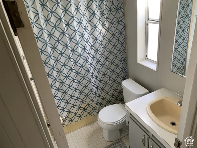 bathroom featuring a vanity with integrated sink, porcelain toilet, vertical window, and tub enclosure