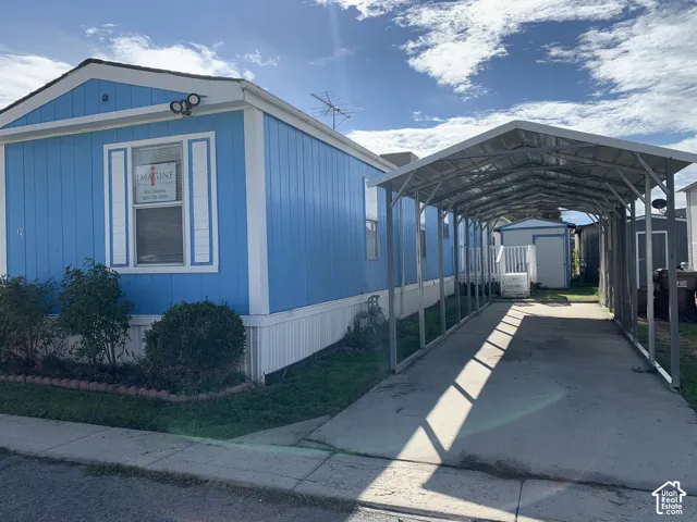 Exterior featuring vertical siding, a metal-framed carport, a concrete driveway, and an attached storage structure