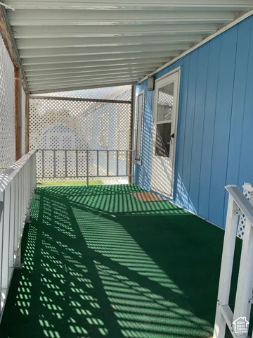 Covered porch featuring a paneled exterior, metal corrugated roof, perimeter lattice fencing, and metal railing