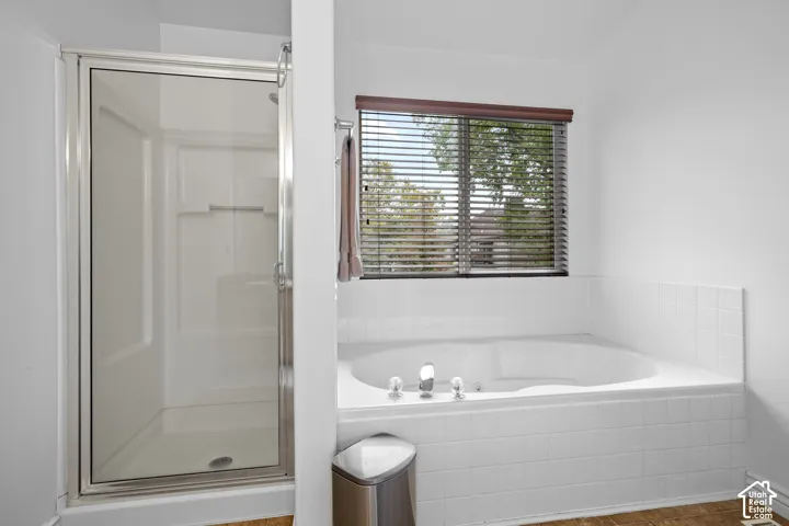 Jetted soaking tub with white tiled surround, glass-enclosed shower stall, and large window with blinds