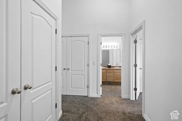 Hallway featuring vaulted ceilings, carpeted flooring, and multiple six-panel interior doors with metallic hardware